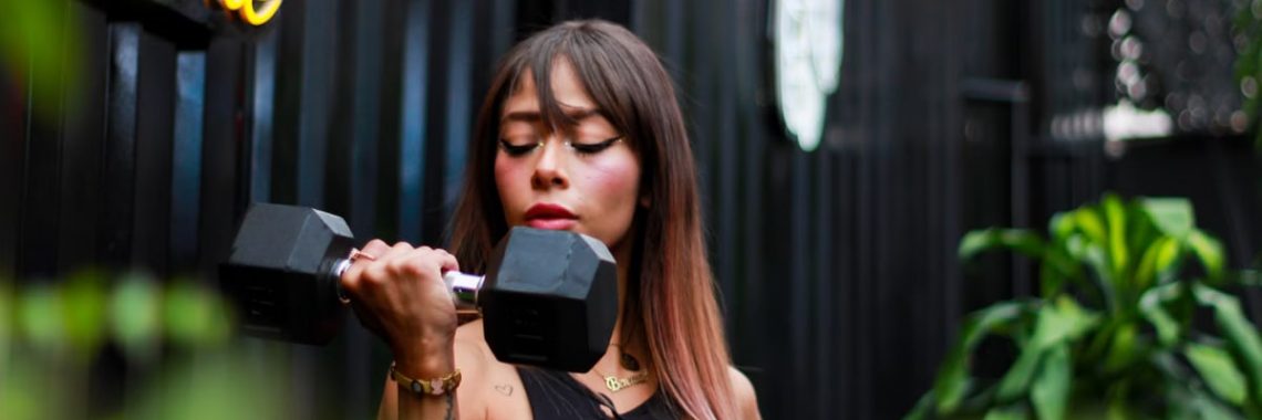 Fitness woman with long hair lifting a dumbbell outdoors, focusing on her strength training.