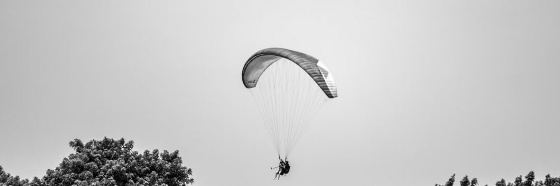A paraglider gracefully glides above the lush trees in Lima, Peru, under a cloudless sky.