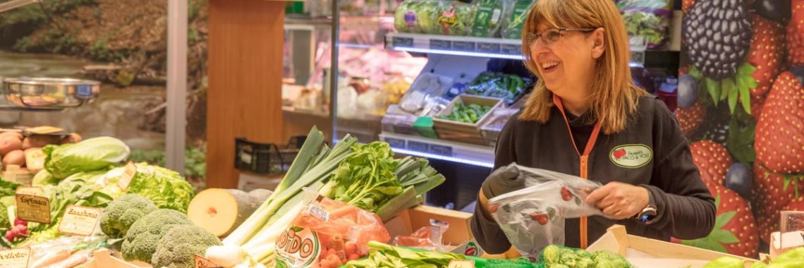 Cheerful woman selling fresh produce at a vibrant market stall. Ideal for promoting local grocery shopping and healthy eating.